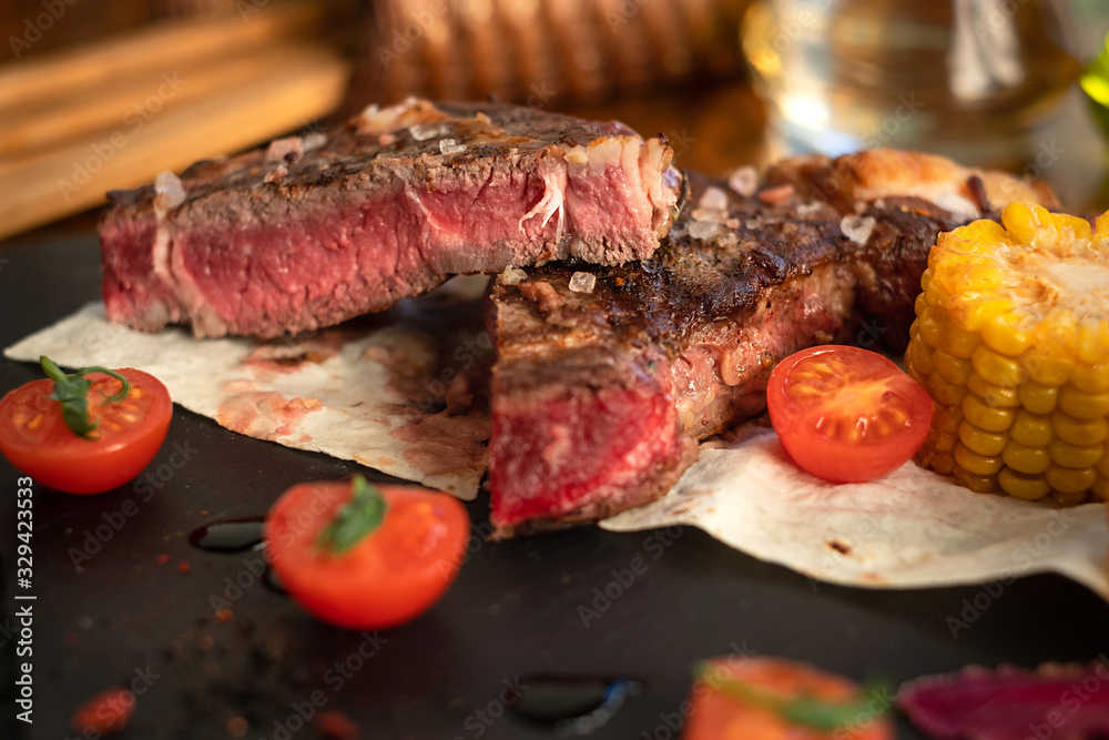 Steak with tomatos and corn on plate on wooden table
