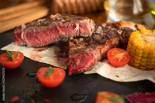 Steak with tomatos and corn on plate on wooden table