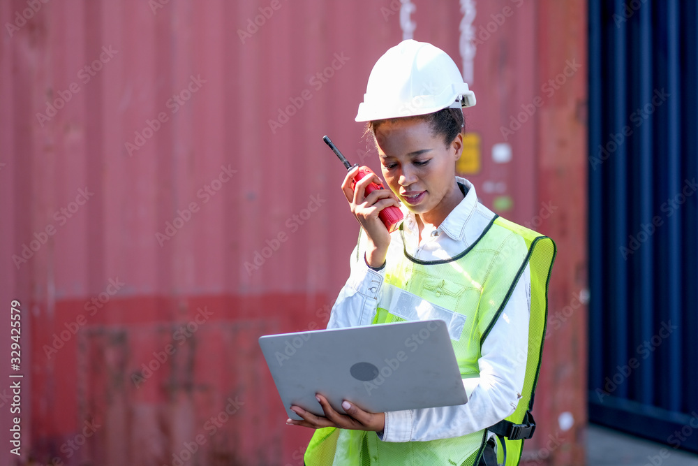 Portrait of African worker woman hold walky-talkie and laptop for her working in cargo container shipping area. Portrait of African worker woman hold walky-talkie and laptop for her working in cargo container shipping area.