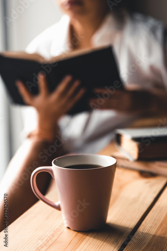 Woman in the morning drinks coffee and reads old book in a white shirt. Education, drink. manicure