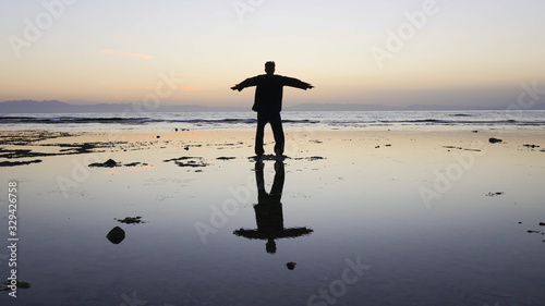 Silhouette of man practiceing qigong exercises at sunset by the sea.