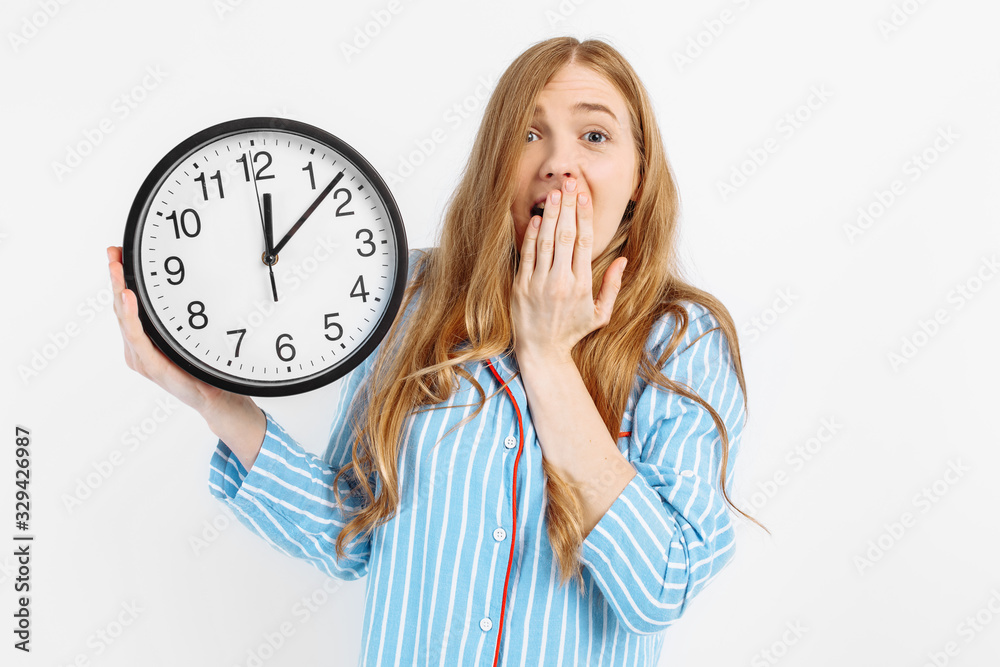 shocked beautiful girl dressed in pajamas showing alarm clock isolated on white background shocked beautiful girl dressed in pajamas showing alarm clock isolated on white background
