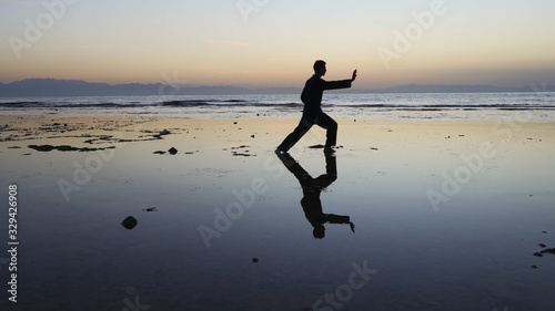 Silhouette of man practiceing qigong exercises at sunset by the sea photo