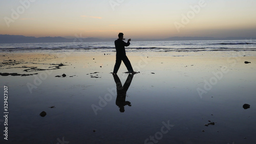 Silhouette of man practiceing qigong exercises at sunset by the sea