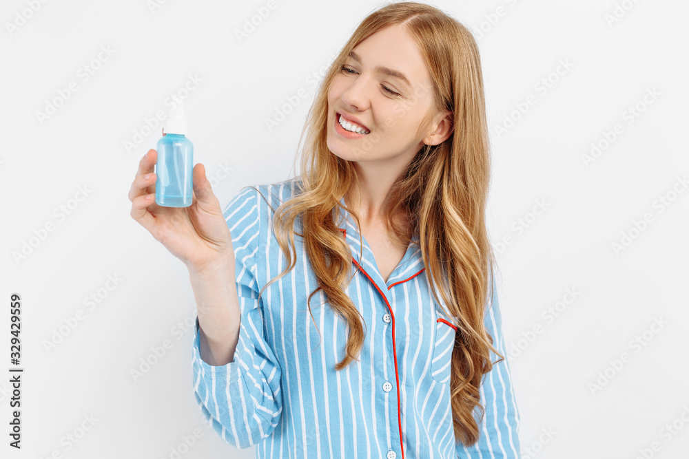 Portrait of happy beautiful young woman in pajamas posing on white background holding hair care bottle Portrait of happy beautiful young woman in pajamas posing on white background holding hair care bottle