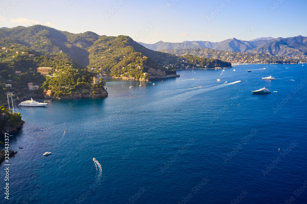 Yachts and boats are sailing in the Ligurian Sea on the mountain background, Portofino, Italy. Rocks and hills seaside with the traditional Italian houses on the top.