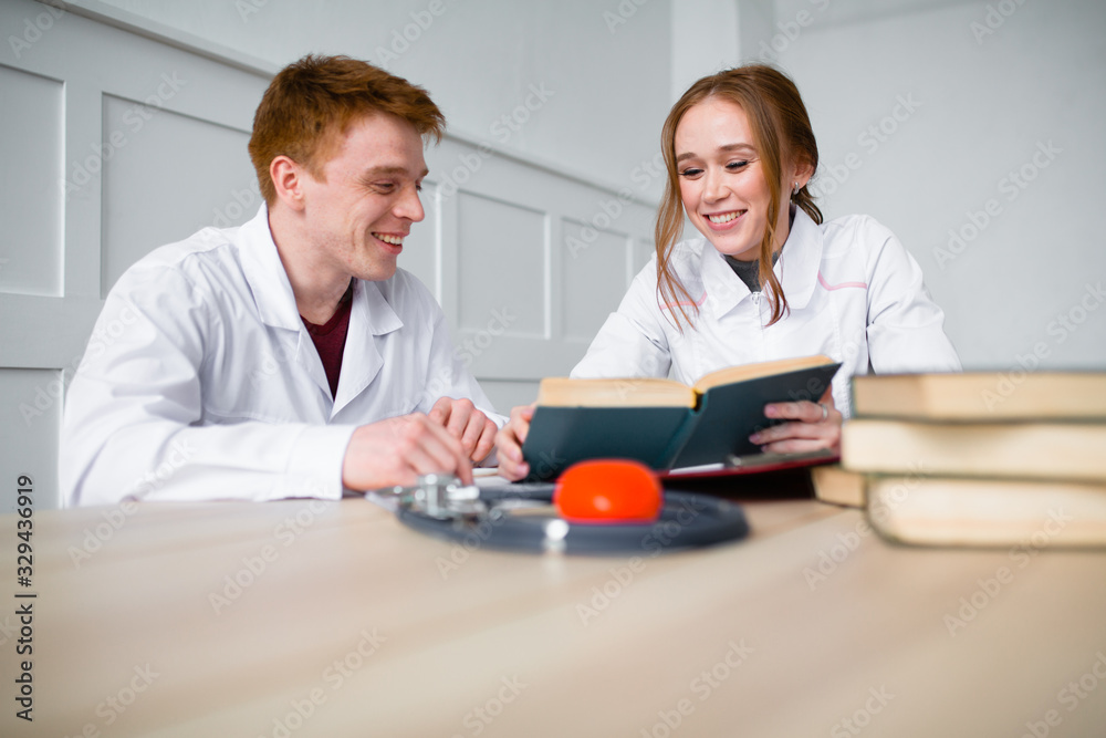 Obraz premium Two doctors are studying medical guidance in search of a cure for coronavirus. Discussion of treatment in a residency among books.