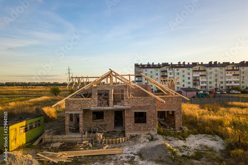 Private residential house with wooden roof frame structure under construction. Unfinished brick building under development.