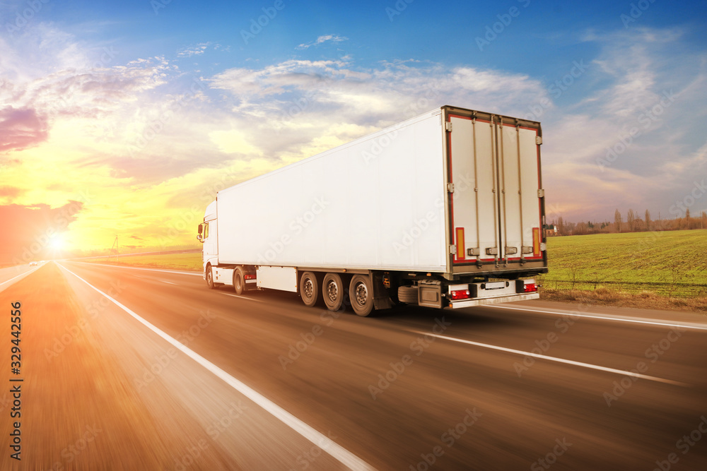 A big truck and a trailer on the countryside road in motion against a sky with a sunset A big truck and a trailer on the countryside road in motion against a sky with a sunset