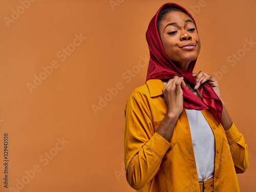 Concentrated woman in a yellow shirt ties a red scarf on her head by hands. Fashion concept photo