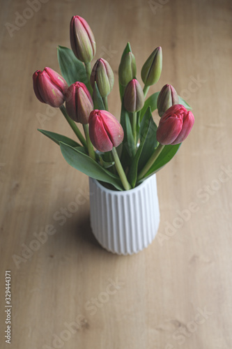 Red tulip flower bouquet on a white pot on a wooden surface