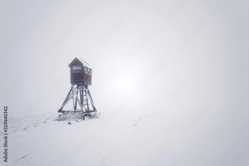 Deer stand, wooden hunters high seat hide on snow covered field, winter foggy day Deer stand, wooden hunters high seat hide on snow covered field, winter foggy day