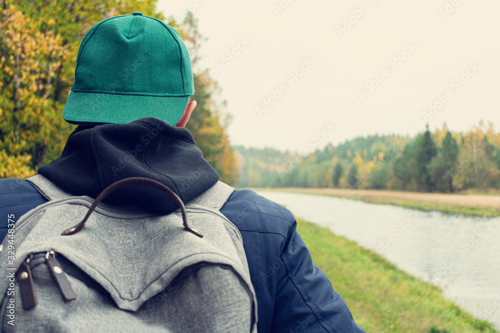 Concept of travel and active lifestyle. Person with a backpack walking along the river, rear view, closeup Concept of travel and active lifestyle. Person with a backpack walking along the river, rear view, closeup