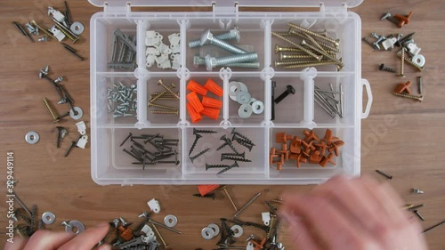Timelapse of hand putting and organizing screws, nails, bolts and washers into a transparent plastic organizer box on a table