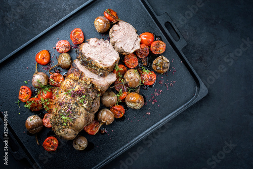 Traditional barbecue rolled lamb roast sliced with tomatoes and mini eggplant as top view on a modern design black tray with copy space