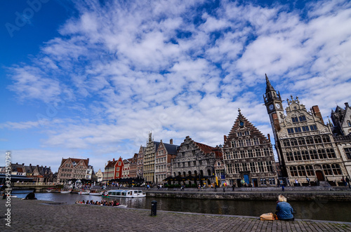 Ghent, Belgium, August 2019. Breathtaking cityscape: from the St. Michael bridge along the Graslei canal. One of the most beautiful postcards in the city. A lady stopped for a break, next to her bags. photo