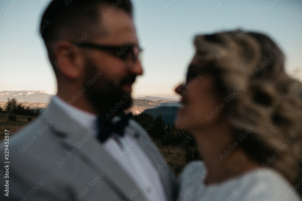 Beautiful couple having a romantic moment on their weeding day, in mountains at sunset. Bride is in a white wedding dress with a bouquet of sunflowers in hand, groom in a suit. Happy hugging couple. Beautiful couple having a romantic moment on their weeding day, in mountains at sunset. Bride is in a white wedding dress with a bouquet of sunflowers in hand, groom in a suit. Happy hugging couple.