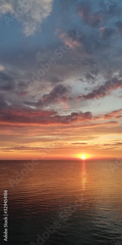 Amazingly vibrant landscape of an alarming dramatic sunset in orange tones. The setting sun is reflected in sea water. Light clouds are painted in different colors from blue to red in the sky