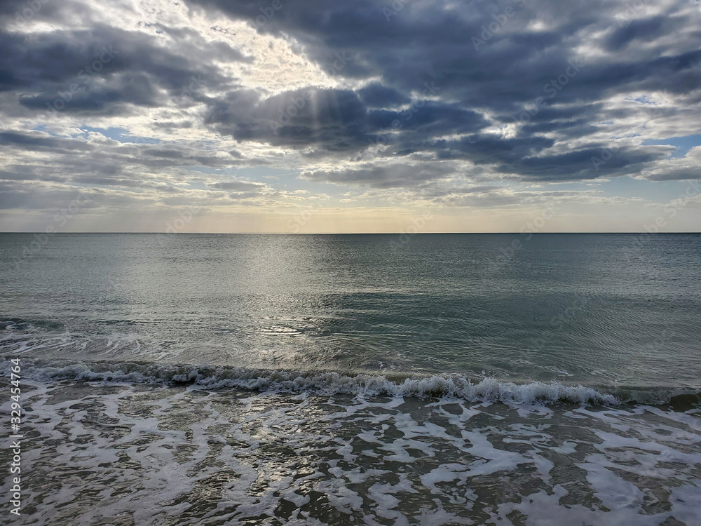 Abstract seascape panoramic background - late afternoon. Calm seas/ocean in the bottom of the frame. Minimalistic simple background image, blue and yellow colors, clouds and sky