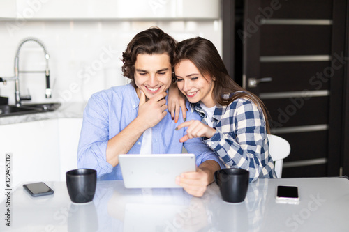 Cheerful young couple having breakfast and using tablet at home