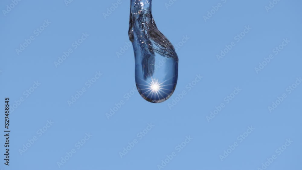 Incredible macro slow motion shot of water dripping from end of thawing icicle melting in spring with sunlight reflected inside. Looping possible.