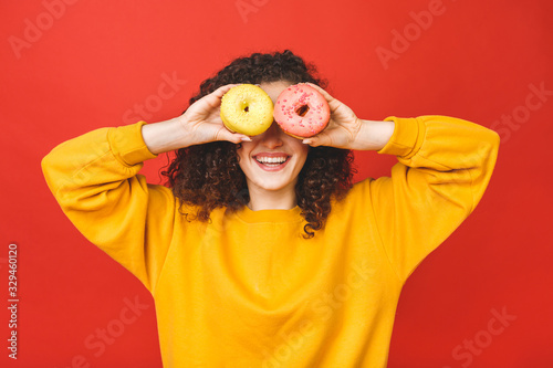 Close up portrait of a satisfied pretty young girl eating donuts isolated over red background.