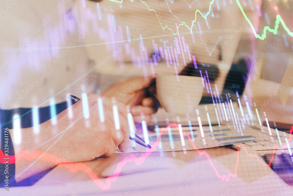 Double exposure of man's hands writing notes of stock market with forex graph.