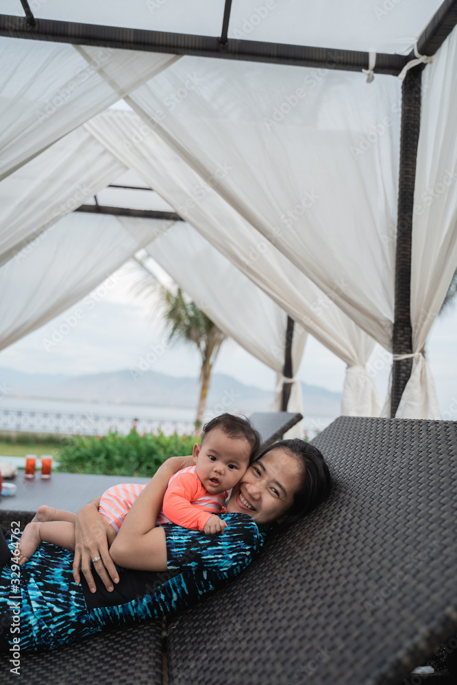 mother hugs her baby when lying on a sun bed by the pool