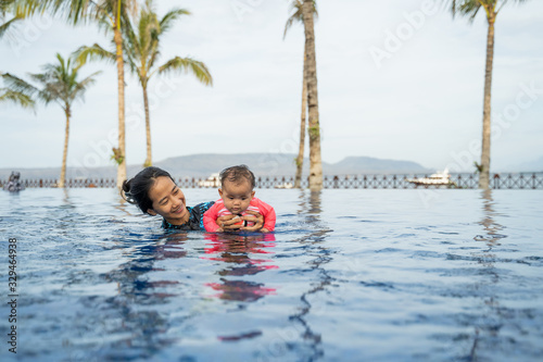 asian mother holds her little baby while swimming and playing in the pool