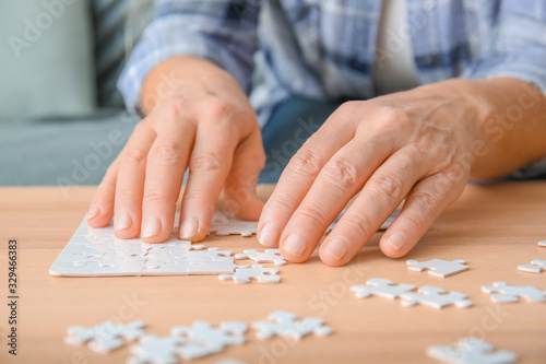 Senior woman suffering from Parkinson syndrome doing puzzle at home, closeup