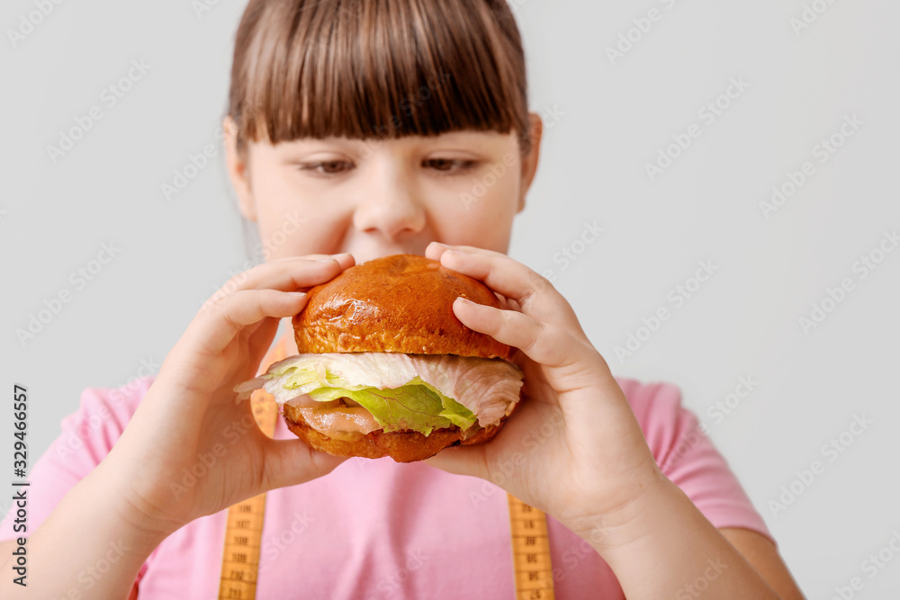 Overweight girl with unhealthy burger on light background