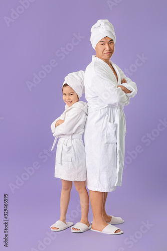 Asian man with his little daughter in bathrobes on color background