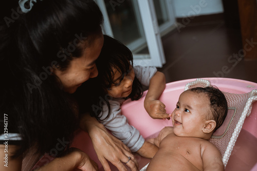 adorable baby having bath with mother and sister, cute baby smiling when take a bath