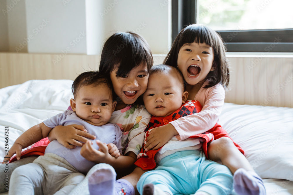 four Asian children laugh while sitting on the bed hugging each other four Asian children laugh while sitting on the bed hugging each other