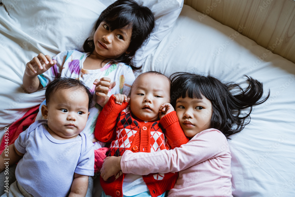 four Asian children lie in bed hugging each other while looking at the camera