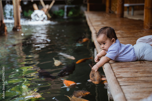 cute little baby while lying looking at koi fish from the edge of the pond