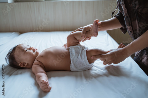 mother holds the feet of a baby child lying in bed giving massage