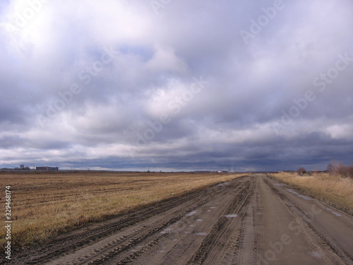 dirt country road in the fields in autumn in cold rainy weather with clouds