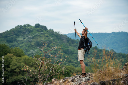 Strong and handsome Caucasian man hiker standing on the mountain peak with outstretched his arms in the air and smiling face. Winning life achievement, freedom and successful business goal concept.