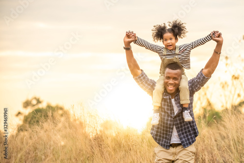 Happy Mixed race African family little child girl sitting on her father neck while hiking on the mountain at sunset with smiling face. Parent and kid enjoy and having fun in summer vacation