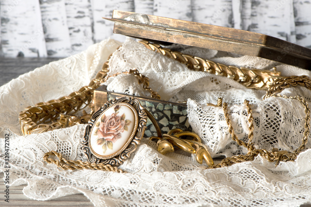 Metal Open Jewelry Box with pile of golden jewelry and lace against wood background Metal Open Jewelry Box with pile of golden jewelry and lace against wood background