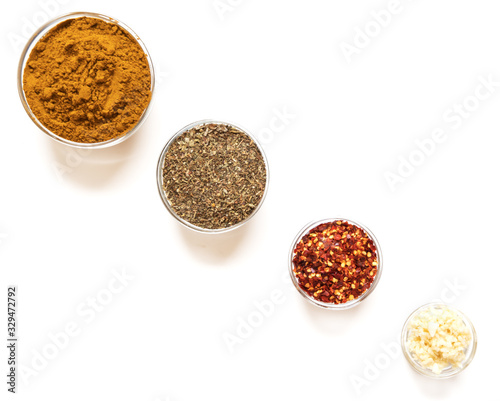 various spices in glass bowls on white background. Top view copy space. Culinary Concept with curry, italina herb mix, crushed pepper and garlic
