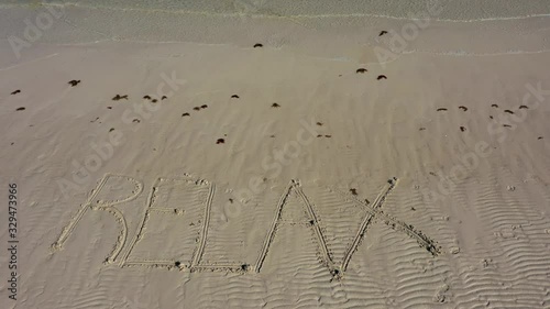 RELAX very small in the frame, inscribed in the sand on a beach as water laps onto the beach. photo