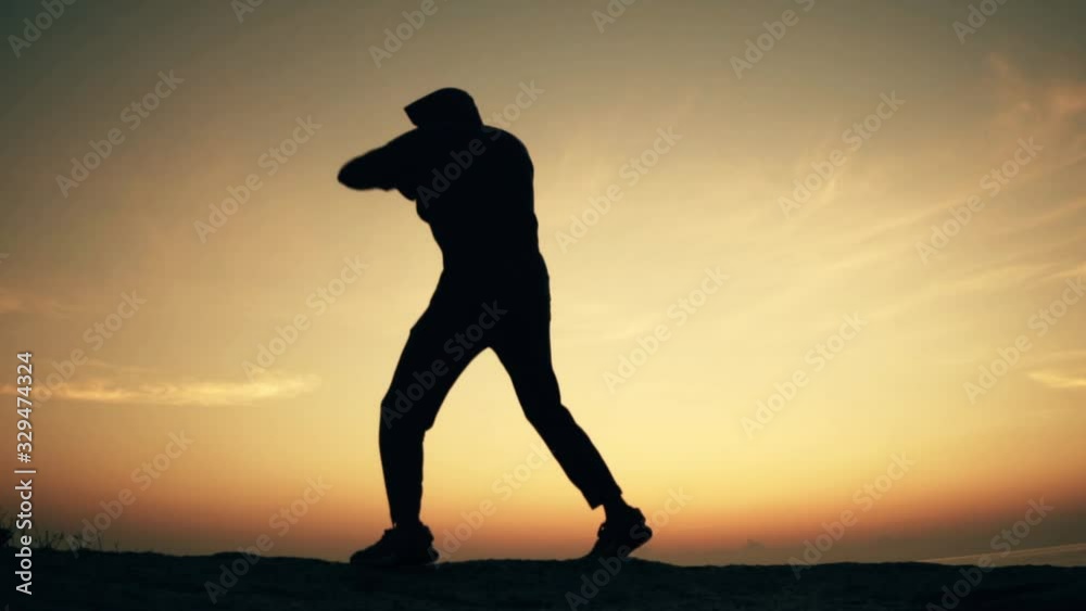 Man practices shadowboxing on a rock by the sea at dawn Man practices shadowboxing on a rock by the sea at dawn