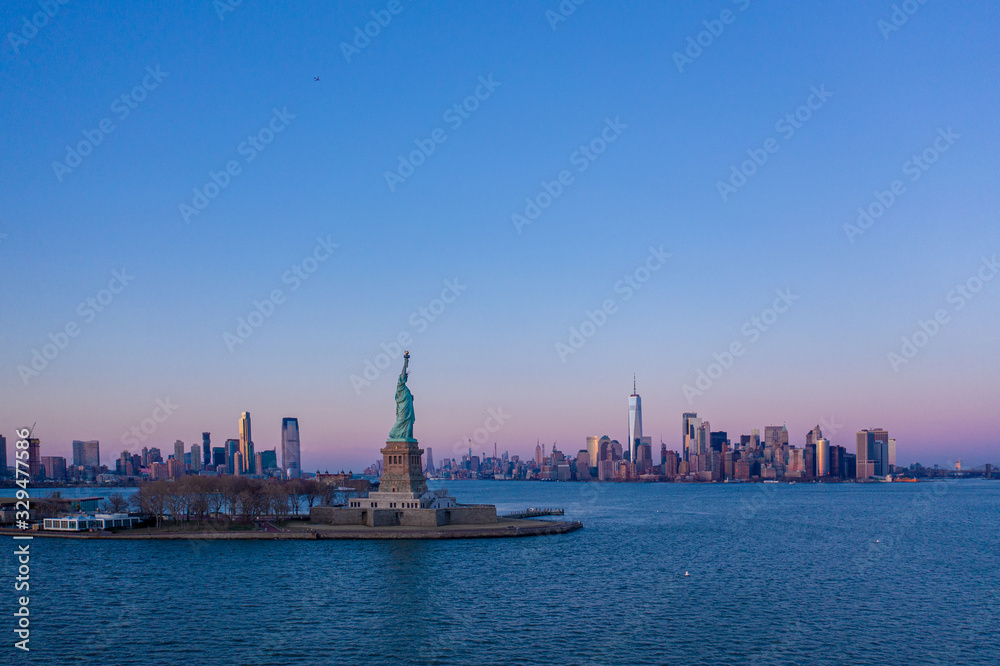 Statue of Liberty and New York Manhattan cityscape in background at sunset, USA