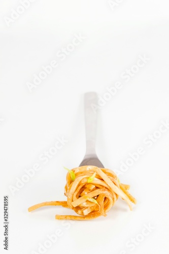 Classic spaghetti carbonara with cream and tomato sauce on fork. Shallow depth of field. Spaghetti on light background. Eating spaghetti requires fork.