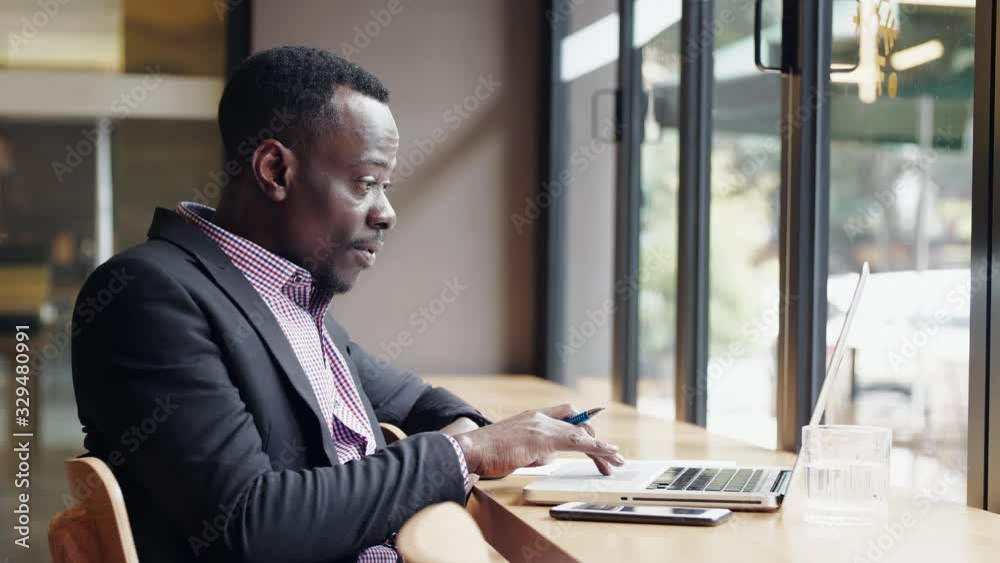 Slow motion of African businessman using laptop in the cafe office by the window getting surprise great good news feel so happy thumb up to the computer screen video meeting online Slow motion of African businessman using laptop in the cafe office by the window getting surprise great good news feel so happy thumb up to the computer screen video meeting online