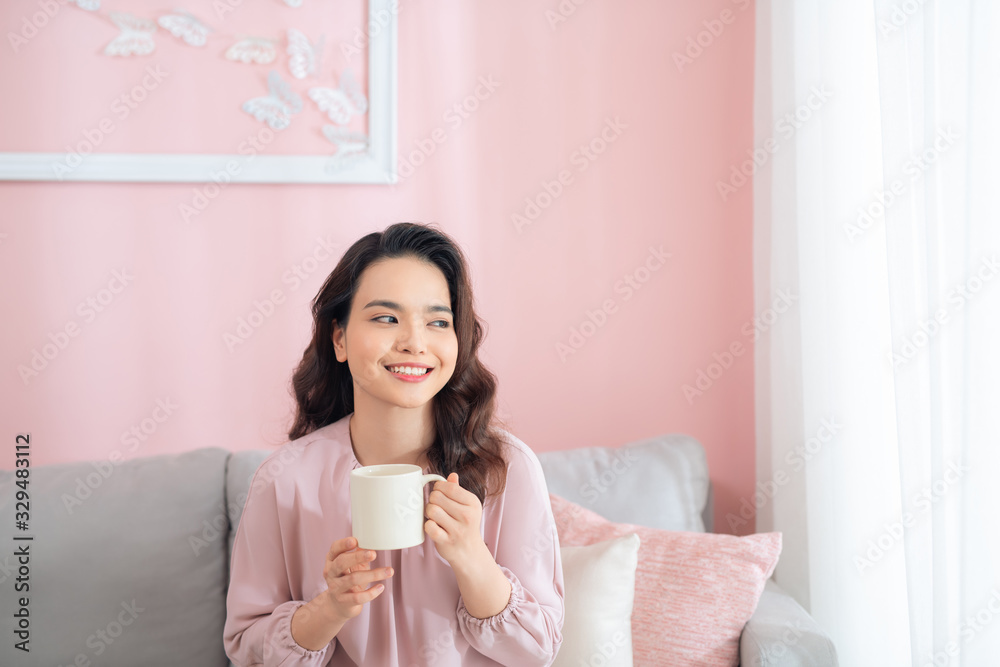 Attractive young Asian woman drinking coffee when sitting on sofa.
