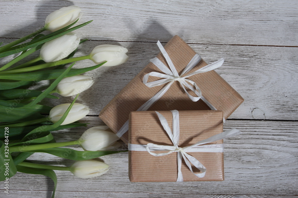 White tulips and gift boxes on wooden table. Women day concept. White ribbon, craft wrap, 8 march, spring, wedding, decoration White tulips and gift boxes on wooden table. Women day concept. White ribbon, craft wrap, 8 march, spring, wedding, decoration
