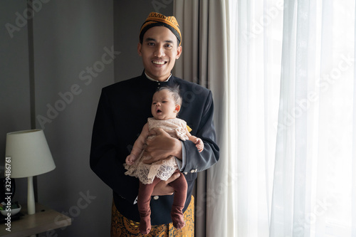Asian man wearing traditional clothes and carrying little daughter,beskap is traditional heritage clothes from Java,Indonesia